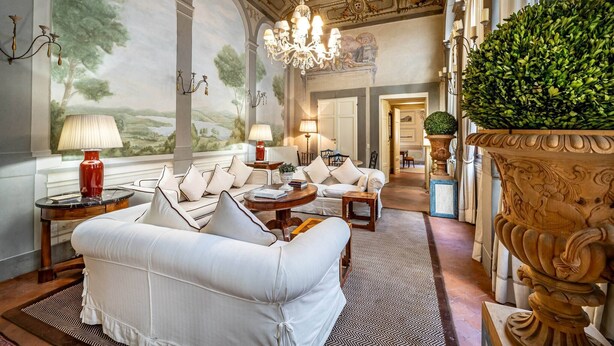 A luxurious room with a white sofa set, a chandelier, and a large decorative plant. - YID Bargello luxury suite (Firenze)