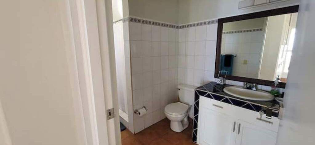 A bathroom with white tiles, a toilet, a sink, and a mirror.