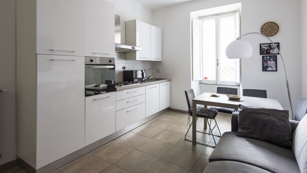 A modern kitchen with white cabinets, a dining area with a table and chairs, and a sofa. - Cosy Vatican Apartment (Roma)