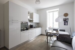 A modern kitchen with white cabinets, a dining area with a table and chairs, and a sofa. - Cosy Vatican Apartment (Roma)