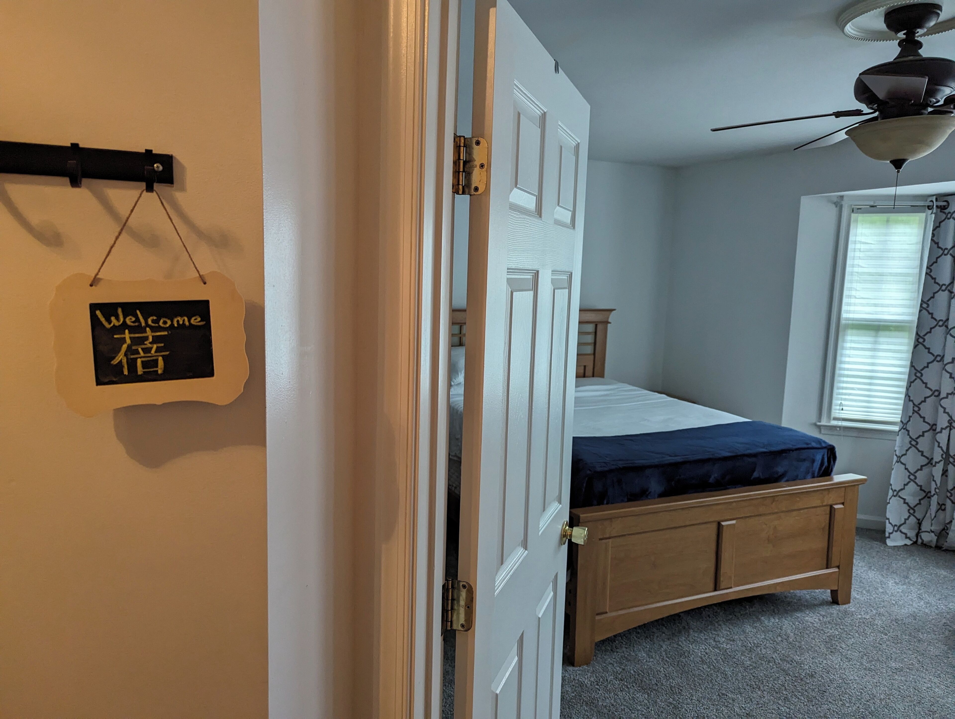 Un dormitorio con una cama, un aparador de madera, un ventilador de techo y una ventana con persianas.