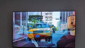 Un téléviseur à écran plat est fixé au mur et affiche l’image d’un taxi jaune dans une rue de la ville. En dessous du téléviseur, on aperçoit une cheminée où les flammes sont bien visibles.