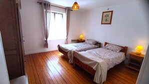 A bedroom with two single beds, wooden flooring, a window with curtains, a wall-mounted picture, and bedside lamps. - LA MADELEINE - MALANDRY (MALANDRY)
