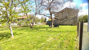 A grassy backyard with a stone wall, a barbecue grill, and a table. - LA MADELEINE - MALANDRY (MALANDRY)