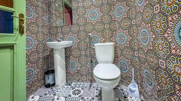 A bathroom with a patterned tile wall, a green door, a white sink, and a white toilet.