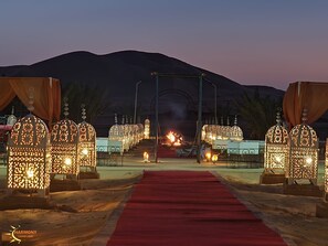 A pathway leading to a structure with ornate lanterns and a red carpet, set against a mountainous backdrop. - Harmony Merzouga Desert Camp (Rissani)