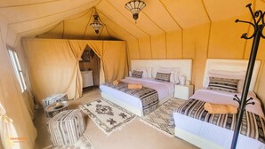 Alojamento em tenda com duas camas, uma mesinha e um candeeiro suspenso.