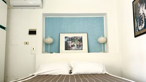 Habitación de hotel con cama, un cuadro enmarcado en la pared, dos lámparas de pared y un pequeño aire acondicionado.