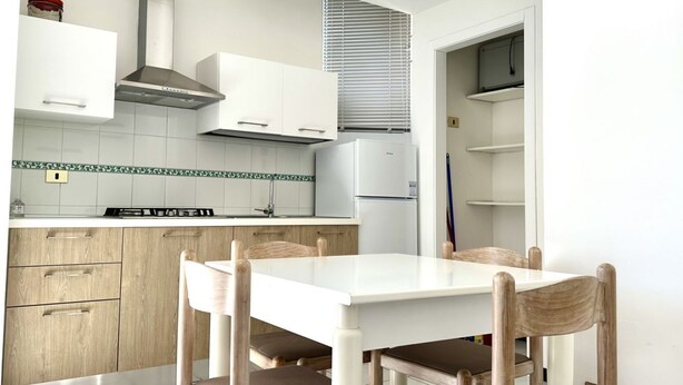 Eine moderne Küche mit weißen Schränken, einem Herd und einem Kühlschrank. Ein Esstisch mit Stühlen steht ebenfalls dort.