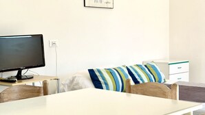 Ein Zimmer mit einem Bett, einem Schreibtisch mit Computerbildschirm, einem Stuhl und einem kleinen, weißen Schrank.