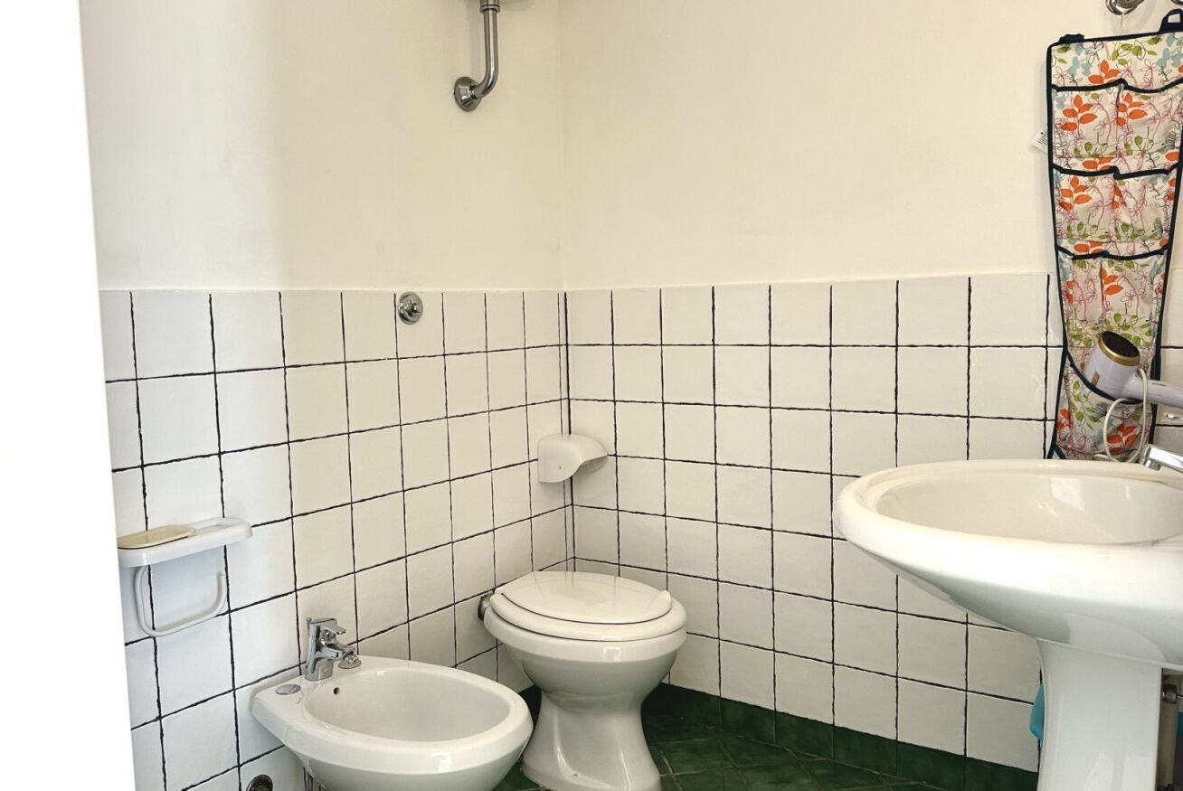 Une salle de bain comprenant des toilettes, un bidet et un lavabo, ainsi qu’un sol carrelé et un rideau de douche.