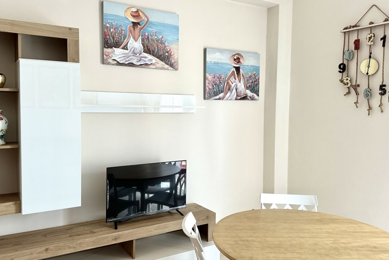A room with a wooden table, a TV on a stand, and two paintings on the wall.