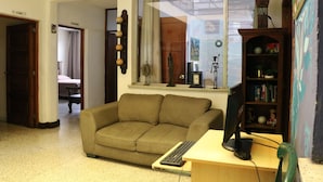A living room with a sofa, a desk with a computer, a bookshelf, and a window with curtains. - Hostal los Volcanes ciudad de Guatemala (Guatemala City)