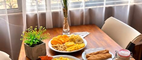 A dining table with plates of food, a vase with yellow flowers, and a view of greenery through a window.