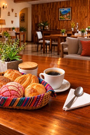 Un coin repas avec une table en bois, un panier de viennoiseries, une tasse de café et une cuillère posée sur une serviette.