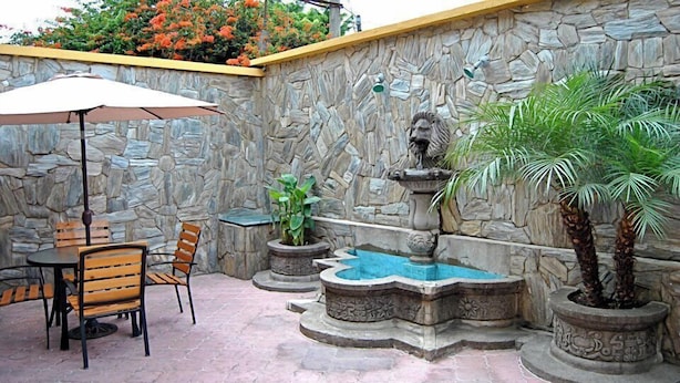 A stone-walled patio with a fountain, a table with chairs, and potted plants. - Hostal los Volcanes ciudad de Guatemala (Guatemala City)