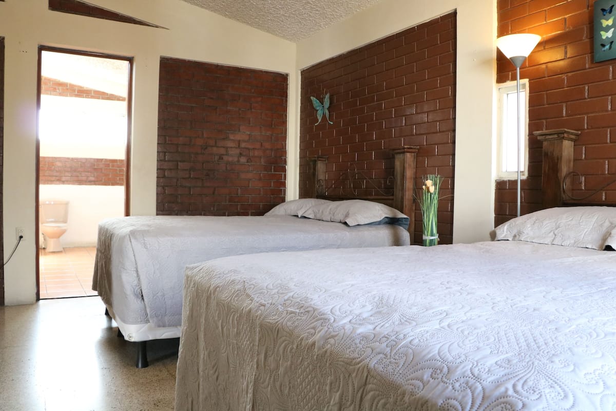 Ein Zimmer mit zwei Betten, einer Ziegelwand, einer Schmetterlingsdekoration und einer Tür, die in einen Außenbereich führt.