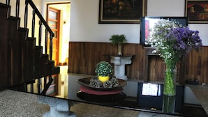 A staircase with a wooden handrail, a dining table with a vase of flowers, and a flat-screen TV on a stand. - Hostal los Volcanes ciudad de Guatemala (Guatemala City)