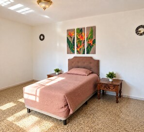 A bedroom with a bed, a headboard, two nightstands with plants, and a wall with a floral painting. - Hostal los Volcanes ciudad de Guatemala (Guatemala City)