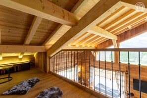 Amplia habitación en ático con vigas de madera, un balcón con barandilla y vistas al exterior.