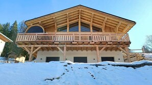 A wooden chalet with a balcony, large windows, and a stone foundation.