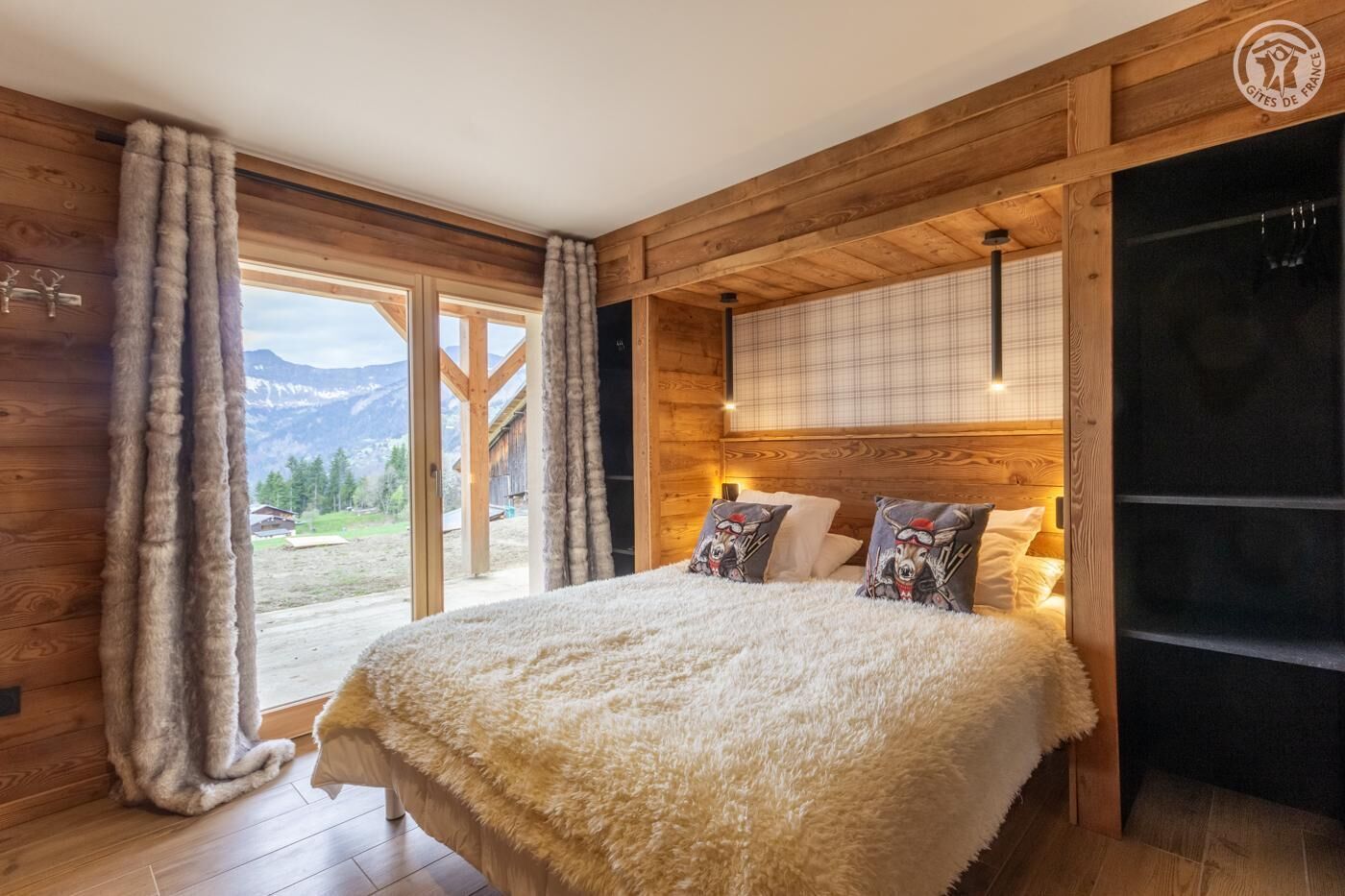 A cozy bedroom with a large bed, fluffy white bedding, and a view of mountains through the window.
