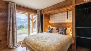 A cozy bedroom with a large bed, fluffy white bedding, and a view of mountains through the window.
