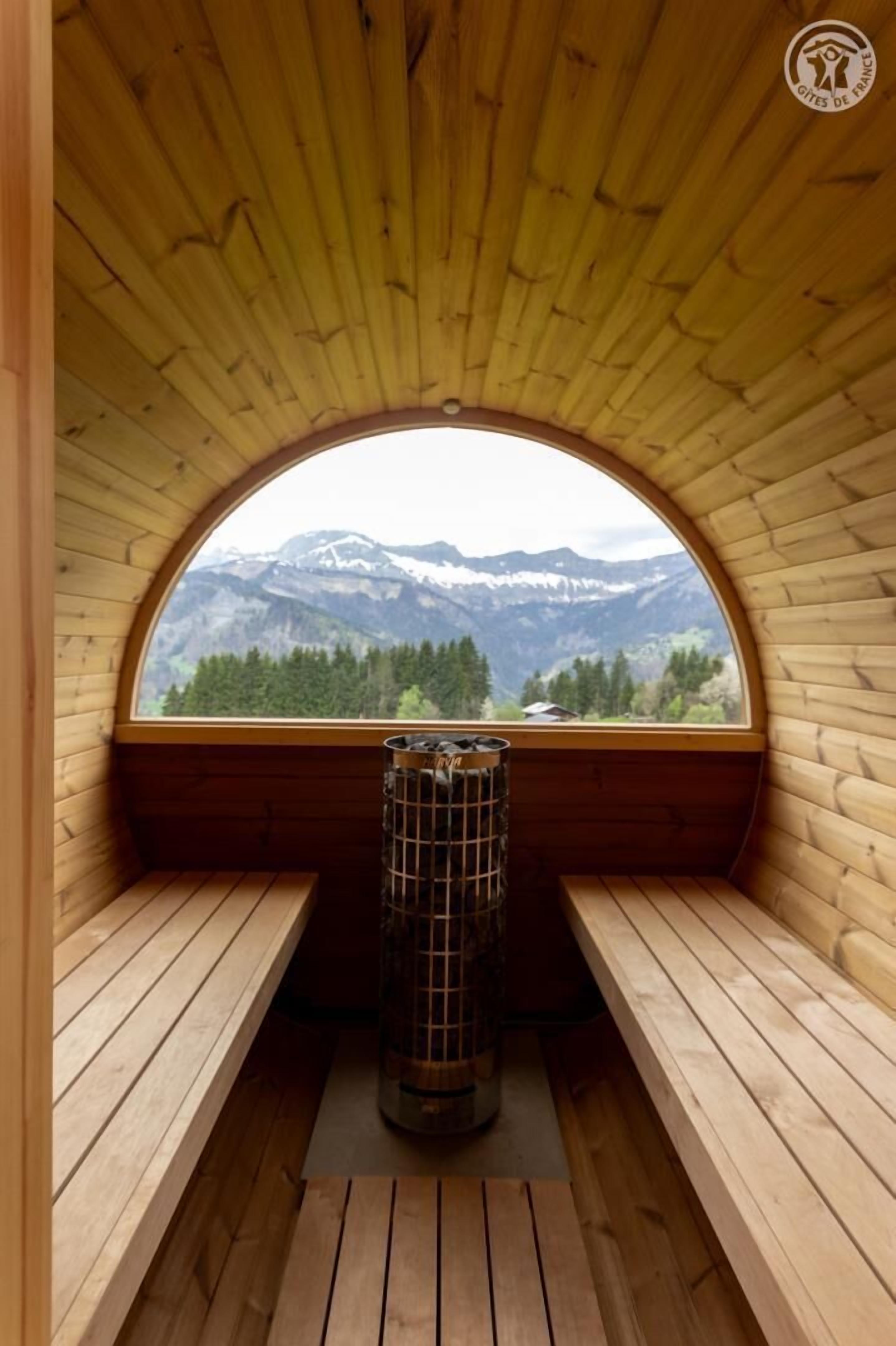 A wooden sauna with a semi-circular window offering a mountain view.