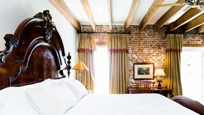A bed with a wooden headboard, a brick wall, and a window with curtains.