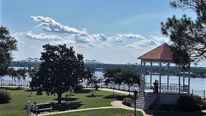 Um gazebo com telhado vermelho com vista para um lago, cercado por um gramado bem cuidado e árvores.