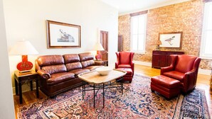 Ein Wohnzimmer mit braunem Ledersofa, roten Ledersesseln, einem gemusterten Teppich und einer Ziegelwand.