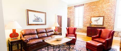 A living room with a brown leather sofa, red leather armchairs, a patterned rug, and a brick wall.