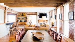 A rustic dining area with a long wooden table and chairs, brick walls, and exposed wooden beams. - The River Walk Inn  - Room 806 (Natchez)