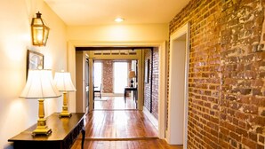 A hallway with wooden flooring, a brick wall, and two lamps on a table. - The River Walk Inn  - Room 806 (Natchez)