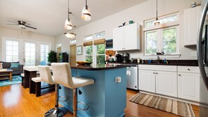 Una cocina moderna con una isla azul, armarios blancos y un área de comedor con sofá gris.