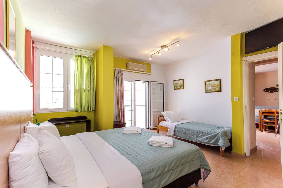 A room with two beds, a window with curtains, a door, and a small table.
