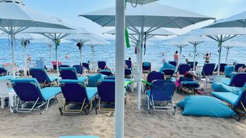 Een strand met rijen blauwe ligbedden en witte parasols, die schaduw bieden aan de strandgasten.