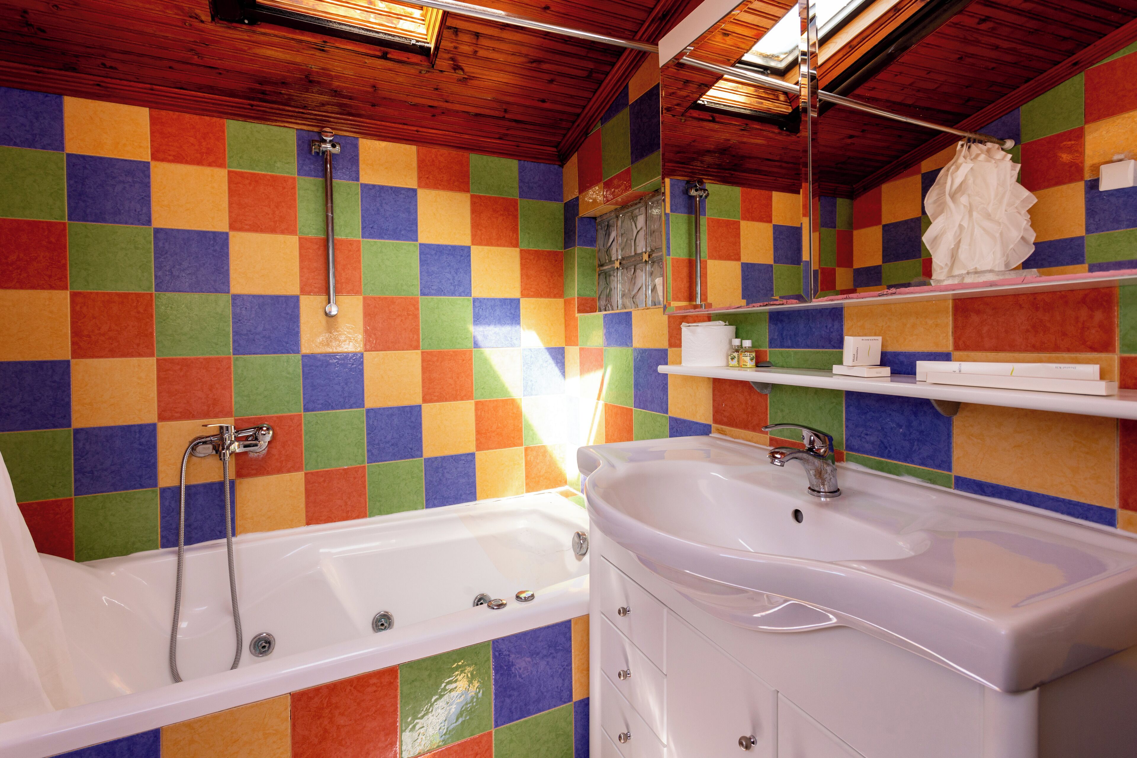Ein Badezimmer mit farbenfroher Schachbrettfliesenwand, einer weißen Badewanne, einem weißen Waschbecken und einer Holzboden.