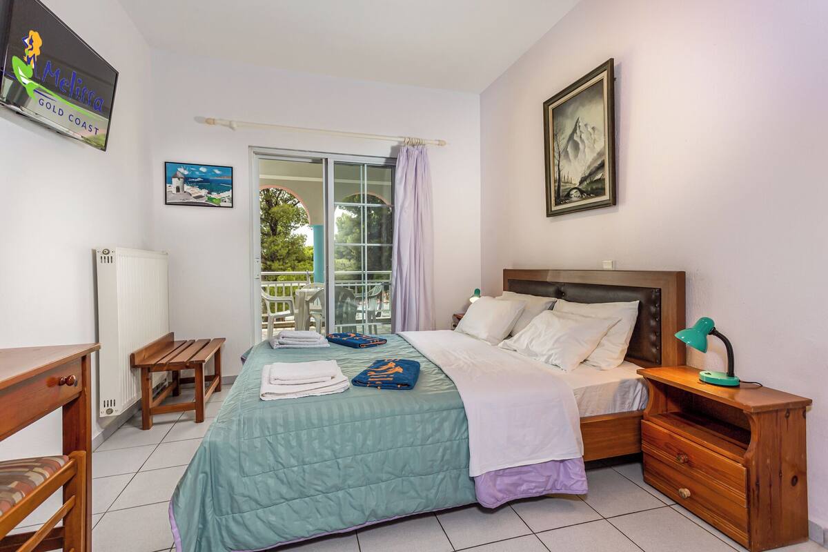 A bedroom with a bed, bedside tables, a desk, a radiator, and a window with a view of the outdoors.