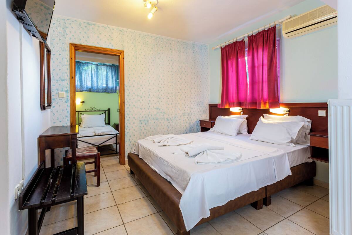 A hotel room with a bed, bedside tables, a chair, a desk, and an air conditioning unit.