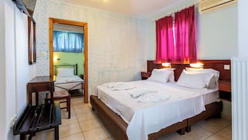 Una habitación de hotel con cama, mesitas de noche, una silla, escritorio y unidad de aire acondicionado.