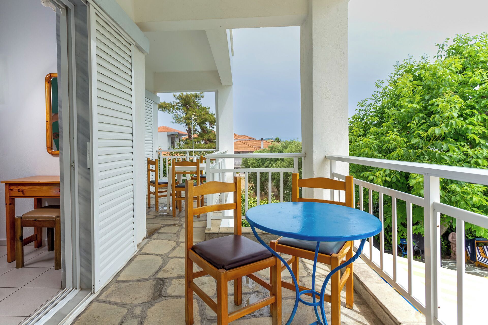 Un balcone con tavolo e sedie, vista sul mare e un edificio con rivestimento bianco.