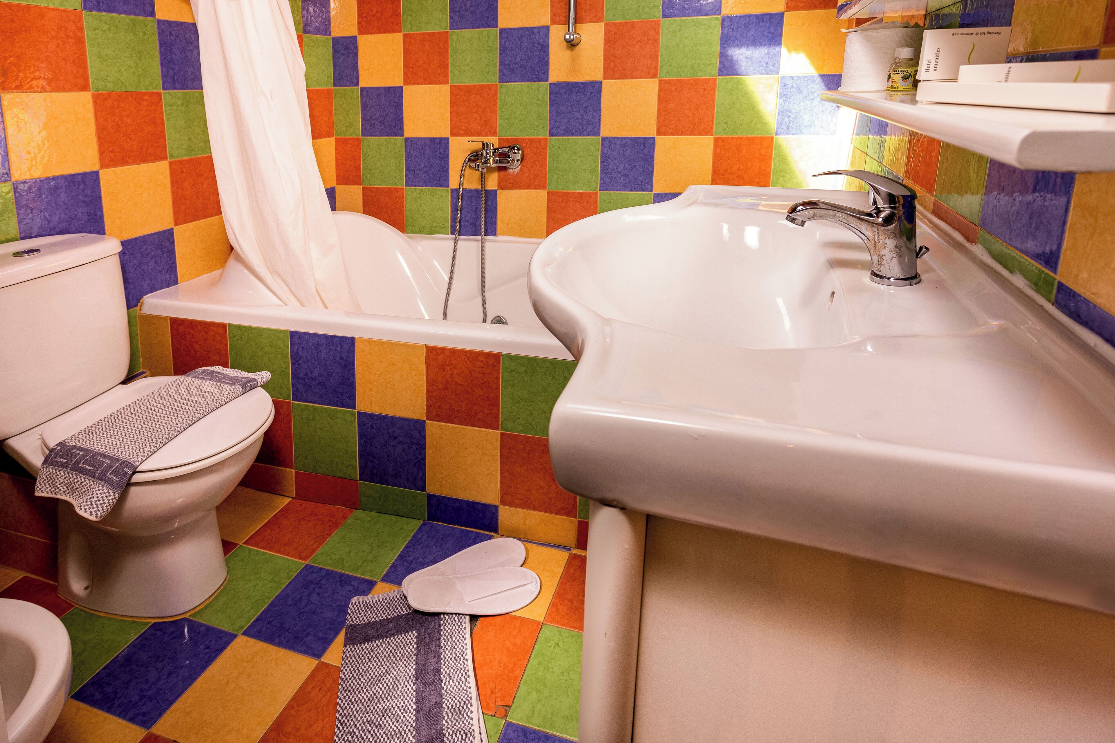 Een badkamer met een vloer in kleurrijke ruitjes, een wit toilet, een badkuip en een wastafel met een kraan.