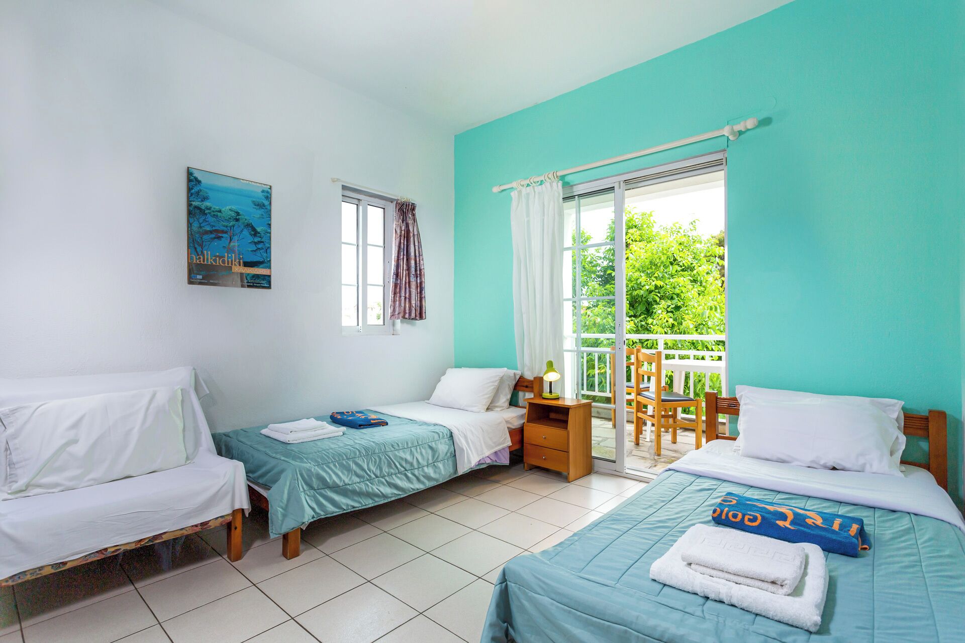 A room with two beds, a window, a door leading to a balcony, and a painting on the wall.