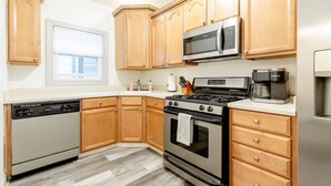 A kitchen with wooden cabinets, a stainless steel dishwasher, a microwave, a stove, and a coffee maker. - Gates Circle 2 Bedroom Sanctuary (Buffalo)