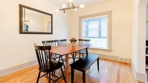 A dining area with a wooden table, black chairs, a mirror, and a window with blinds. - Gates Circle 2 Bedroom Sanctuary (Buffalo)