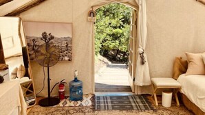 A cozy tent room with a bed, a small table, a fan, and a water bottle.