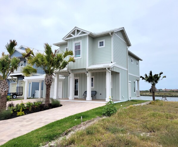 A two-story house with a covered porch, a small deck, and a view of the water. - The Laguna Lady--Lakefront 3 BR House with Private Dock, Minutes to the Beach! (Port Aransas)