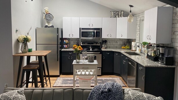 A modern kitchen with white cabinets, a black refrigerator, a microwave, and a stove. There is a dining area with a table and chairs, and a ceiling fan.