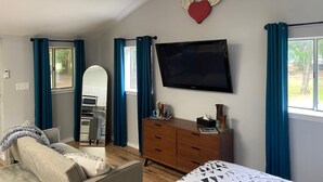 A bedroom with a bed, a dresser, a TV, a mirror, and a window with curtains.